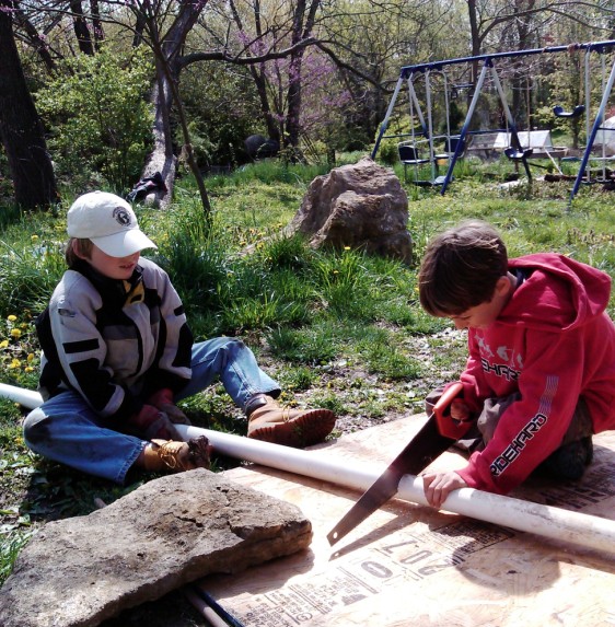 Sawing PVC pipe to roll the plywood with the block on top (note that is just a practice stone, not the super-heavy one they were charged with moving)